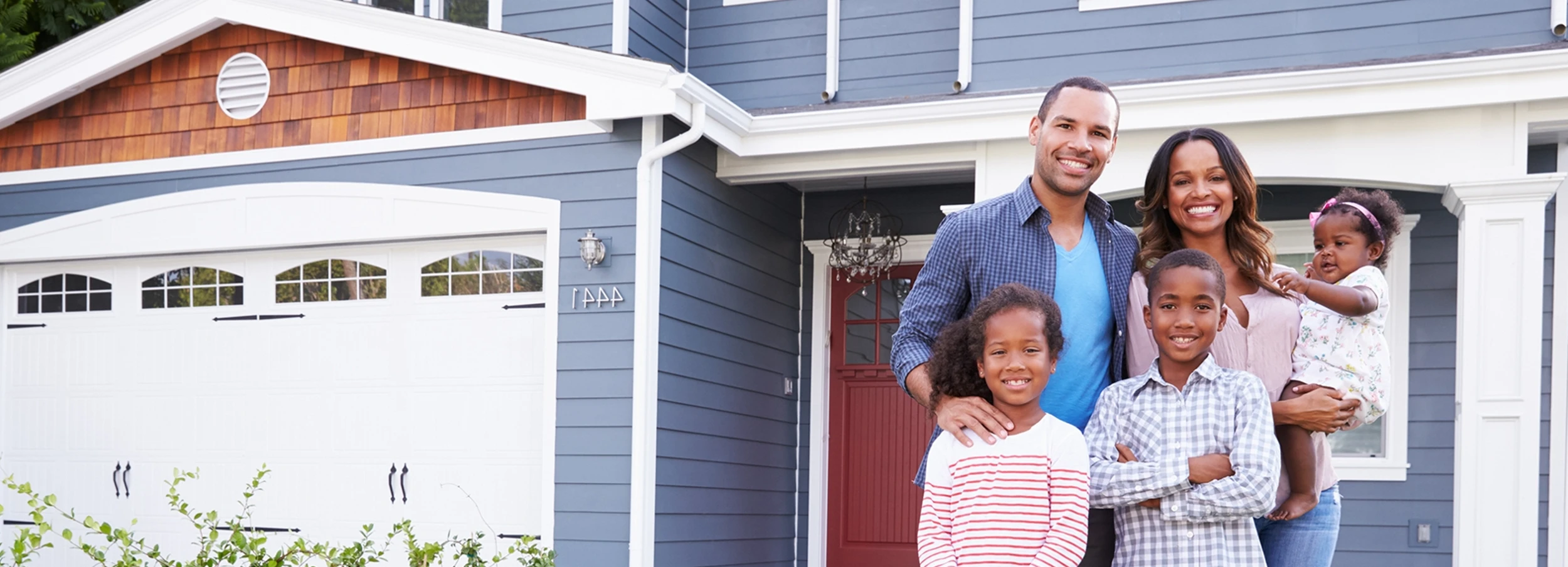 Young African American family smiling in front of two story home with garage.