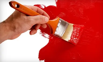 Close-up of man's hand holding a paintbrush and painting a wall red.