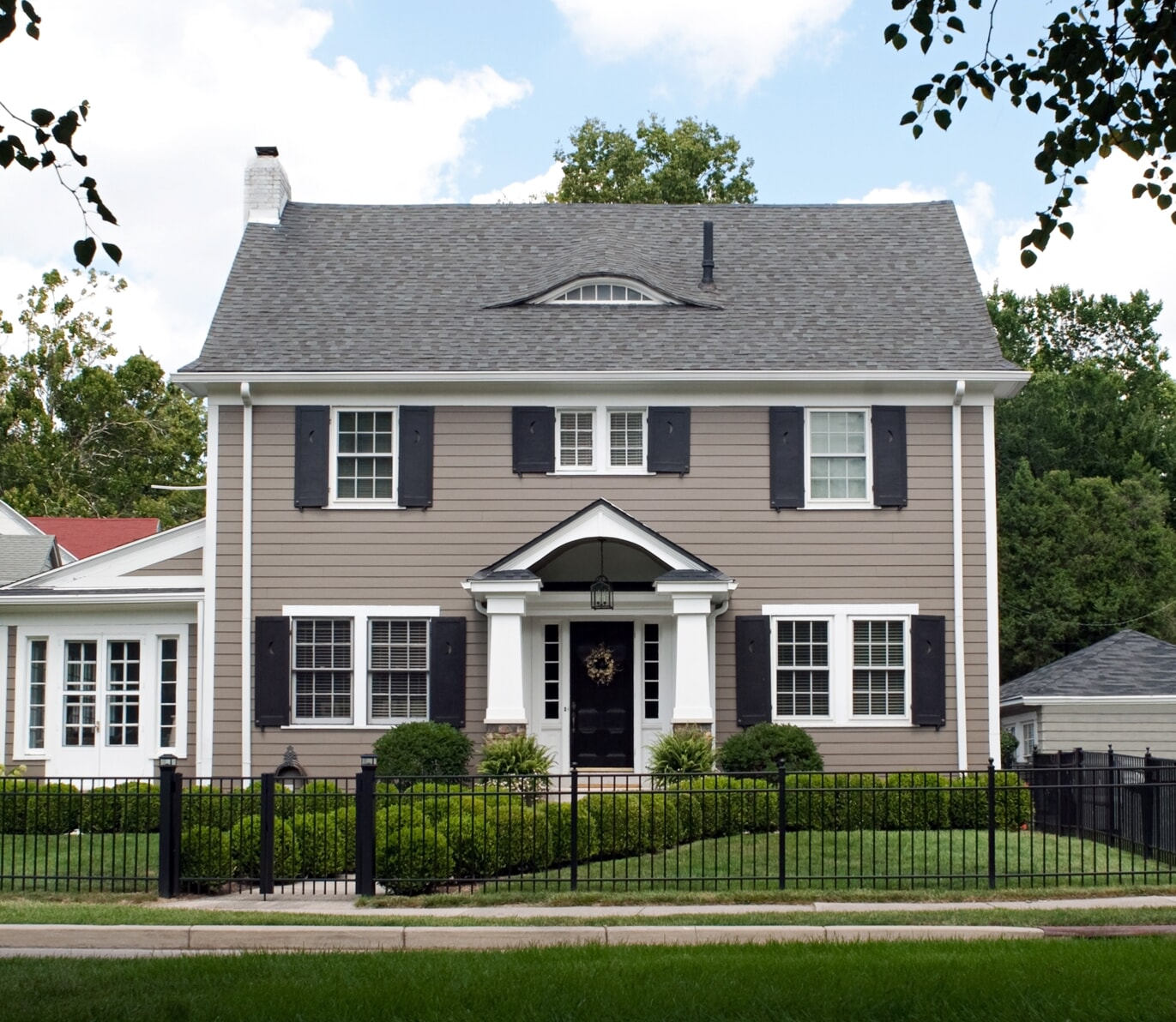 Two story beige home with white trim and black fence