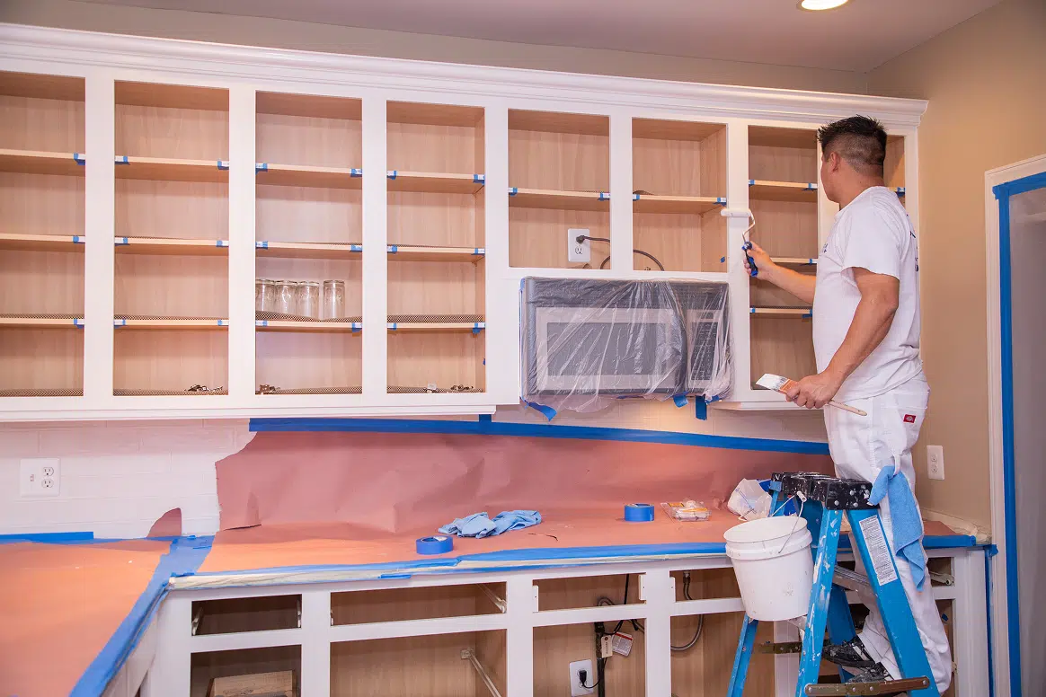A Five Star Painting professional paints kitchen cabinet frames white after carefully masking the counters