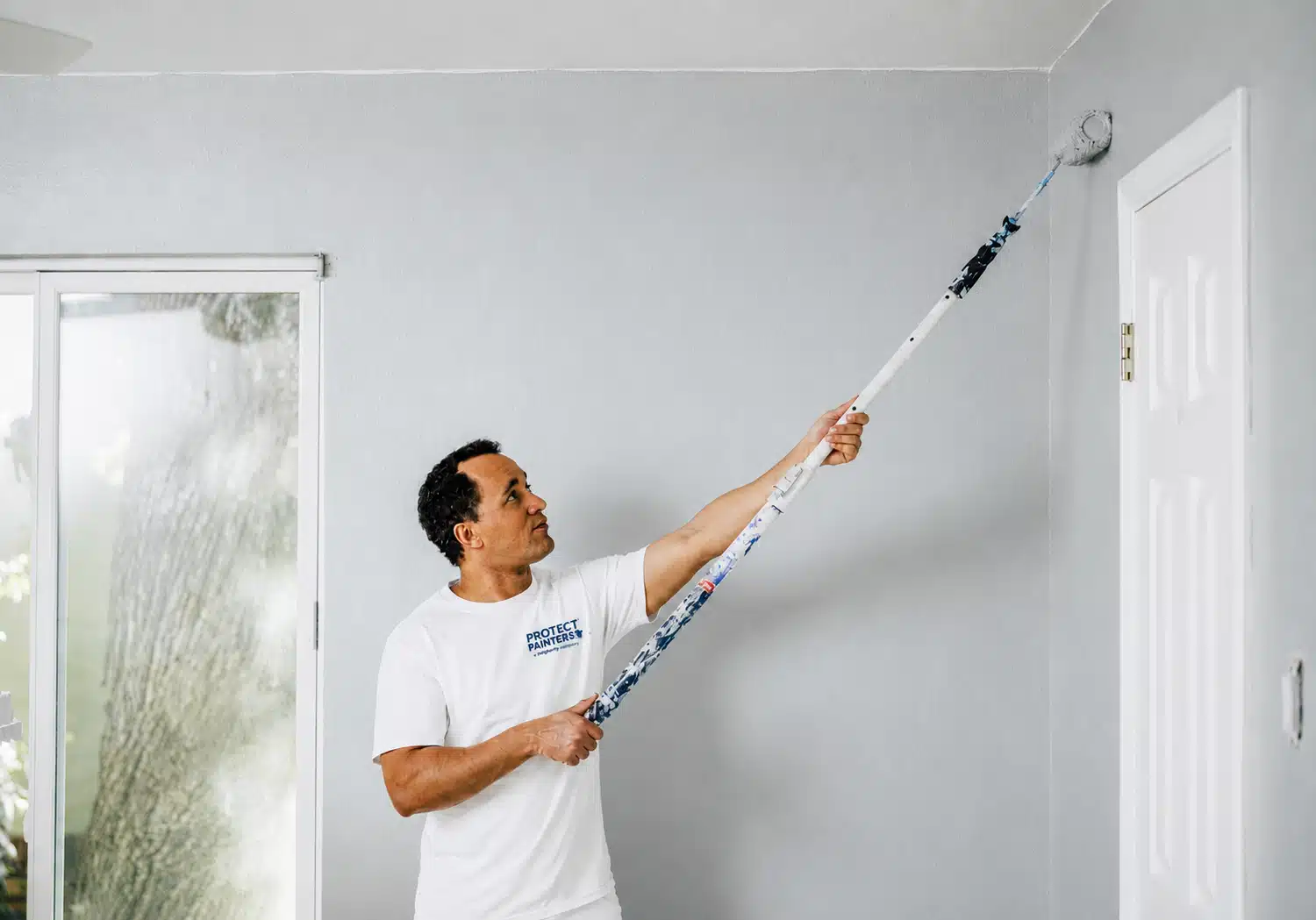 A ProTect Painters professional paints a living room wall light blue for a residential interior painting project