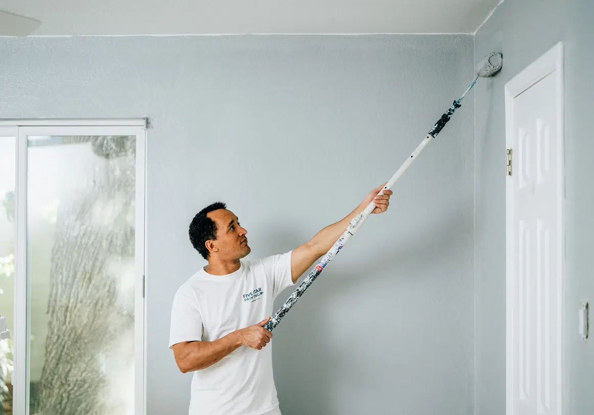 A Five Star Painting professional paints a living room wall light blue for a residential interior painting project