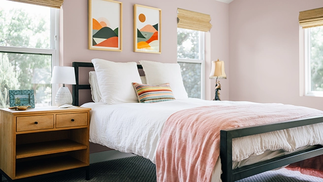Bedroom with a wooden end table, pink comforter and art on pink colored walls.