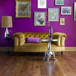 Retro living space with green velvet couch and fuschia walls with wall art.