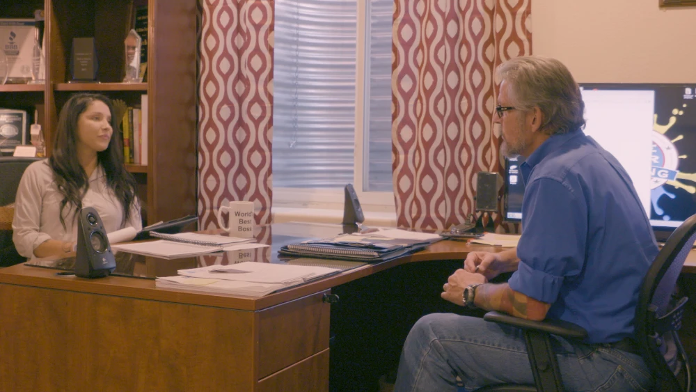 Man and woman sitting on either side of a desk in an office.