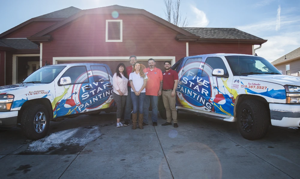 People in a team photo next to two Five Star Painting trucks with a red house in the background.