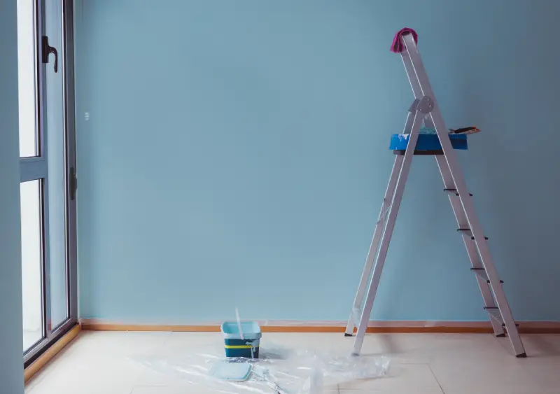 ladder against a freshly painted blue wall with an open paint can at its base