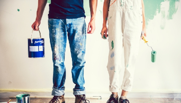 Young couple holding paint can and roller with paint on clothes and shoes