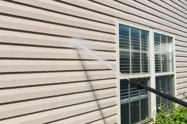 Hose pressure washing vinyl siding of a house.