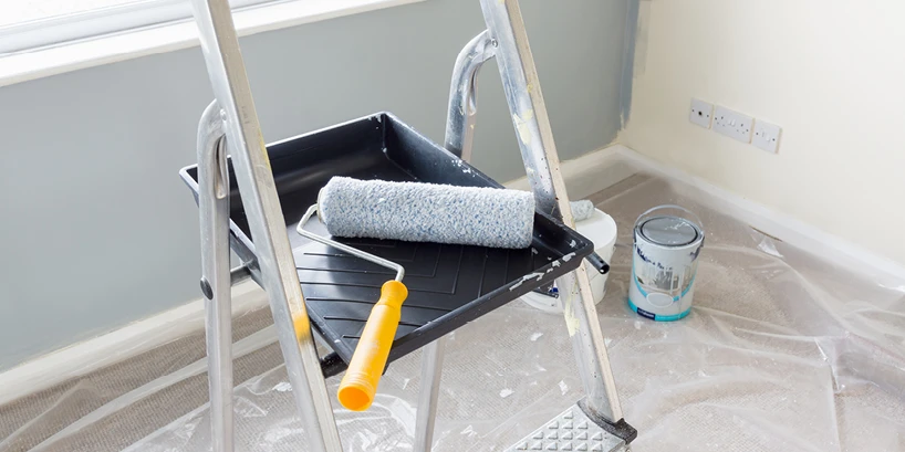 Photo of a room covered in protective plastic, a painting tray and roller brush rests on top of a painting ladder