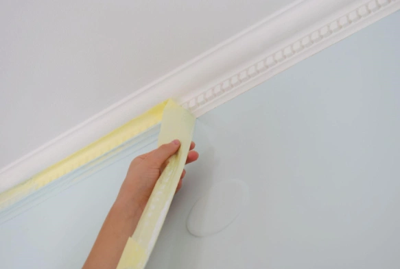 Hand pulling off painters tape masking crown molding on freshly painted wall.