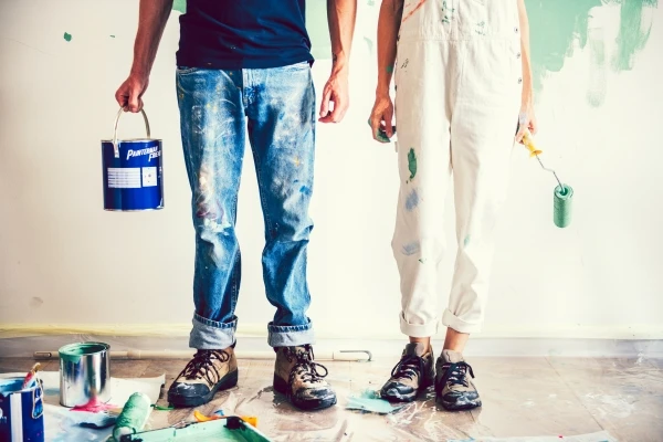 Young couple holding paint can and roller with paint on clothes and shoes