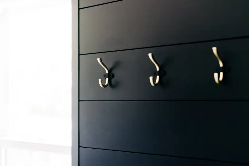 Black painted shiplap interior wall with three silver hooks and window to the left of them.