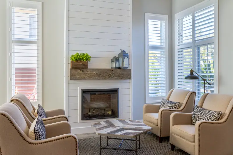 Farmhouse living room with white painted shiplap, electric fireplace, cream walls, tan furniture.