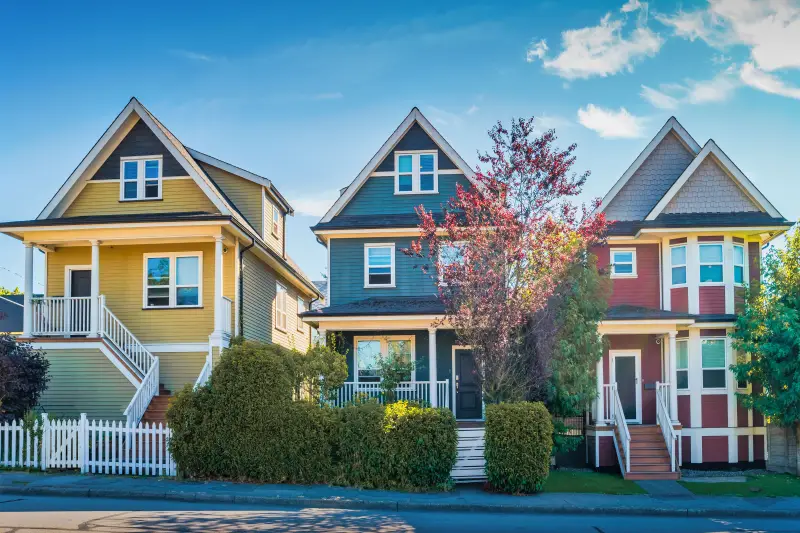 Street view of colorful homes with white trim. Left is yellow, middle is blue, right is red.