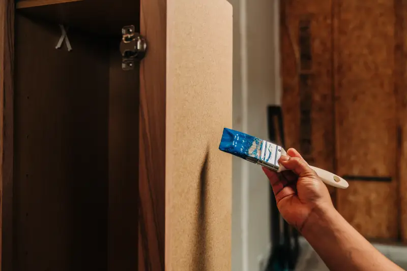 Close-up of someone holding a paint brush with cobalt blue paint up to inside of MDF cabinet door.