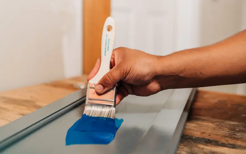 Close-up someone painting a removed, gray polyurethaned cabinet door a bright cobalt blue.