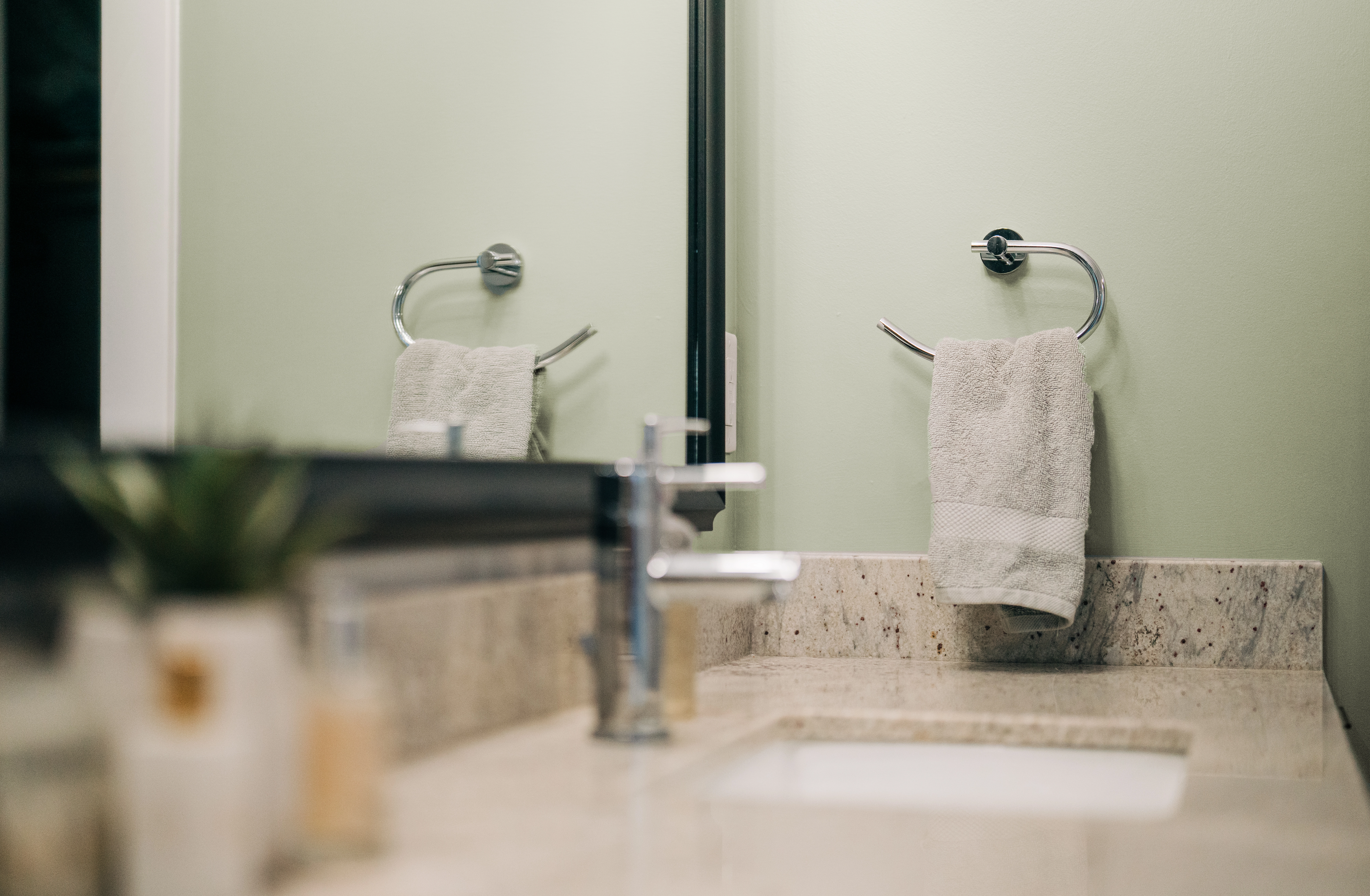 Close-up of tan marble bathroom countertop and light green painted walls with matte sheen.
