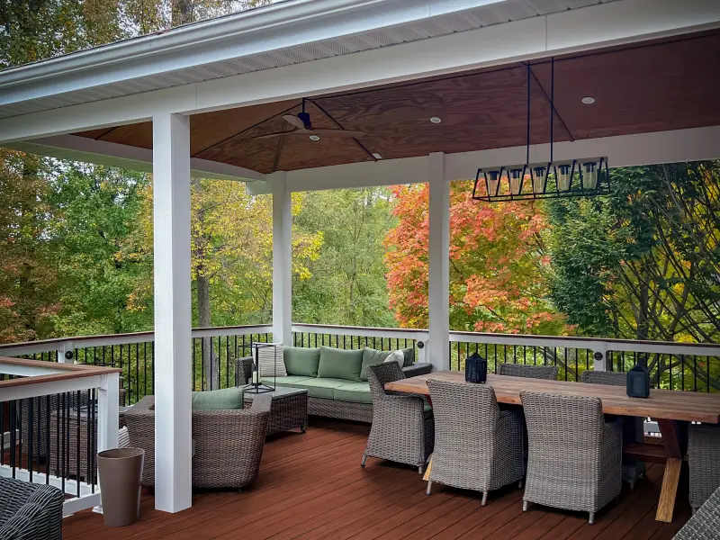 Fenced-in upper deck with wood floor painted rusty red, white railing and trim, wicker furniture.