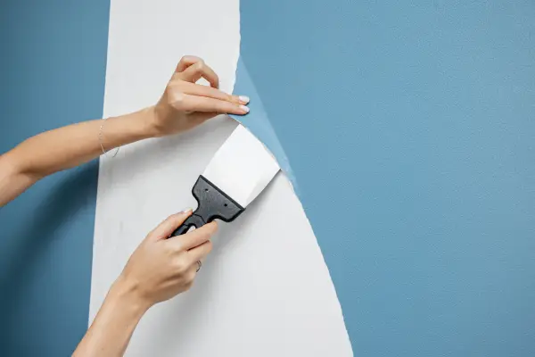 Woman's hands using scraper to remove blue wallpaper.