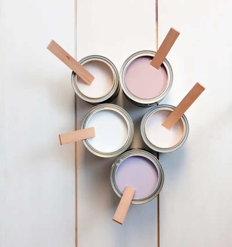 Top down view of open cans of pastel paint. There is a stirring stick inside each can. 