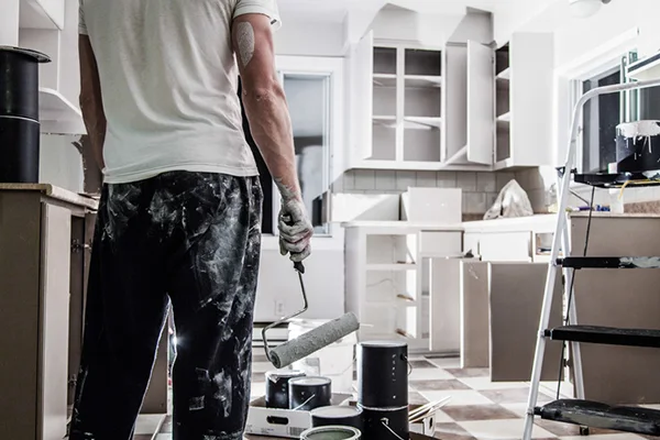 Man holding paint roller inside a white kitchen.