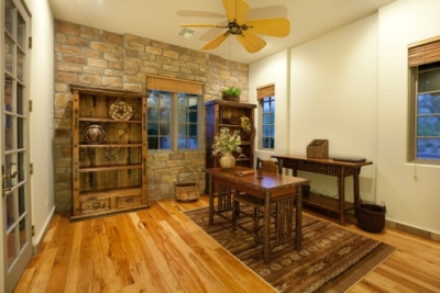 Earth-toned home office with taupe paint, brown brick wall, wooden desk, wooden bookshelves and hardwood floors  