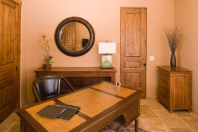 Beige walled office with medium colored wood furniture, dark wood accents and personal touches including a painting, flower arrangements and mirror  