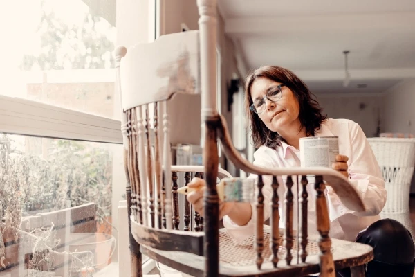 Brown haired woman with glasses painting an antique chair