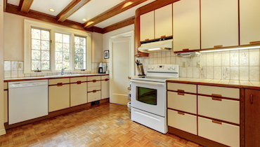 Outdated kitchen with cream colored cabinets and dark wood trim