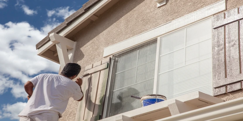 Man in white shirt painting wooden window shutters.