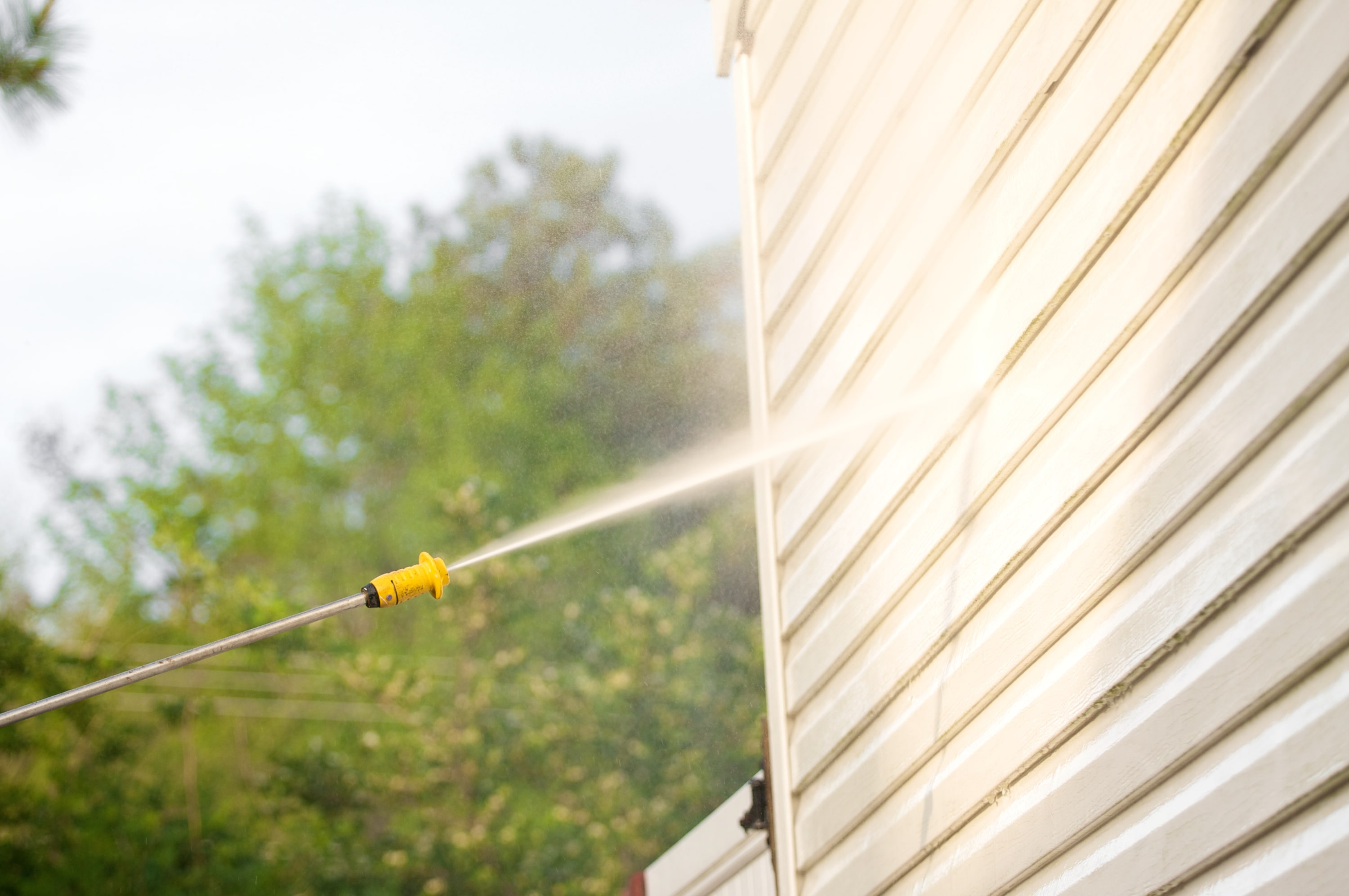 A pressure washer blasting water at the exterior siding of a home.