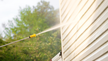 A pressure washer blasting water at the exterior siding of a home.