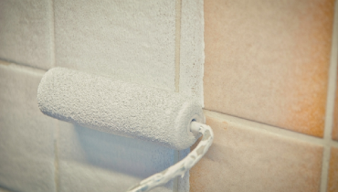 Closeup of small paint roller being used to paint over bathroom tile