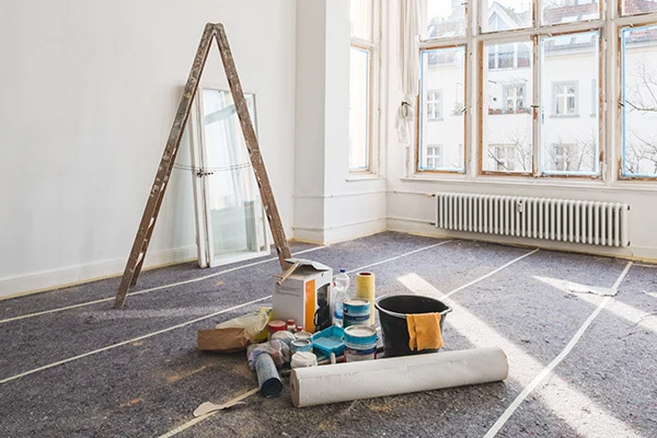 Painting supplies and ladder in the middle of a empty room.