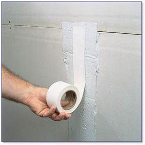 Hand holding drywall tape against the wall