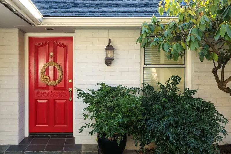 Front of residence with painted white brick and a red door.