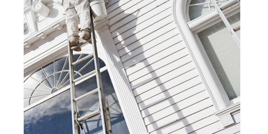 Exterior of a home being painted by a painter on a ladder