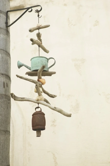 Photo of a hanging mobile made of driftwood, an old watering can, and a cow bell