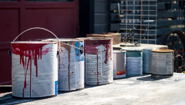 Several old paint cans in front of the garage of a residential home.
