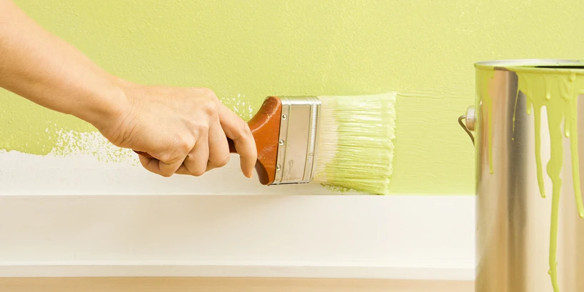 Photo of someone painting a white wall with light green paint