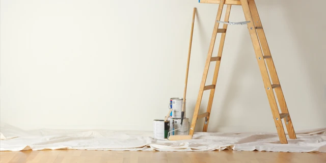 Photo of a ladder and other painting supplies sitting on a tarp covering a wooden floor