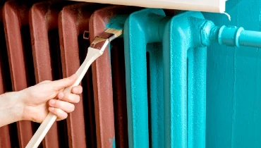 Closeup of a person using a special curved paint brush to paint a radiator.