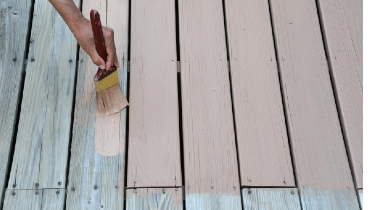 Person using a paint brush to paint a wooden deck