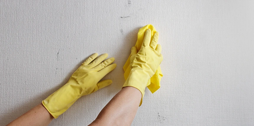 Photo of someone in yellow rubber gloves washing a dirty white wall