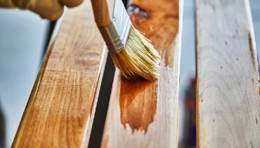 Person applying stain with a brush to a birch wood bench