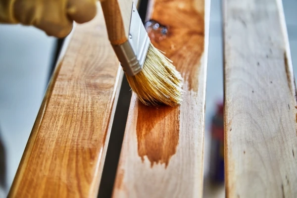 Person applying stain with a brush to a birch wood bench