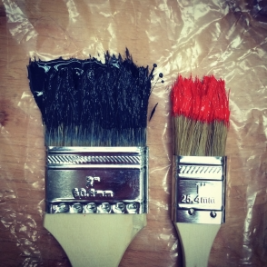Photo of two used paint brushes resting on plastic covered wooden table