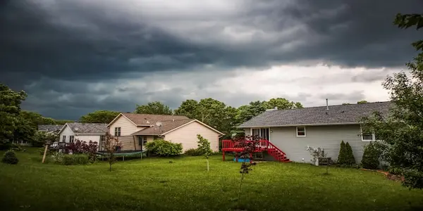 Grassy backyard and several homes under cloudy sky.