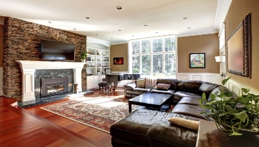 Image of wood floors in living room with fireplace, baby grand piano, and dark brown leather couch.